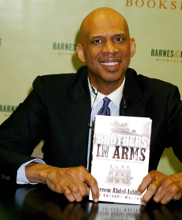 Foto von Kareem Abdul-Jabbar, wie er Exemplare seines Buches *Brothers in Arms: The Epic Story of the 761st Tank Battalion signiert.